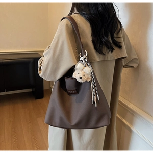 Détail d'un grand cabas en toile marron foncé avec un charm ours en peluche et un pompon décoratif