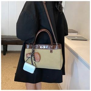 Detail of canvas shoulder bag featuring brown leather trim and unique mini book pendants