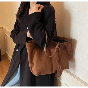Brown suede tote bag side view showing long shoulder straps and knotted charm detail