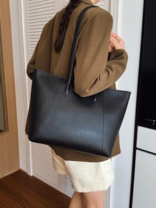 Detailed side view of a large black faux leather tote bag worn as an underarm shoulder bag