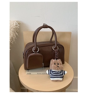 Detail of dark brown leather Boston bag with plush dog charm on a wooden table