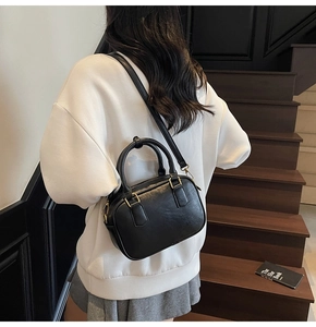 Detail of a vintage black crossbody bag with gold hardware worn by a model in a lifestyle setting