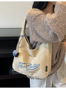 Beige canvas hobo tote bag with blue embroidery shown on a model for daily use