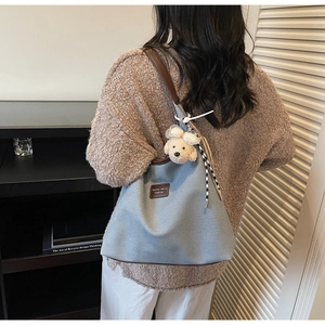 Détail du sac cabas en toile gris-bleu avec lanières en cuir et breloque ours peluche
