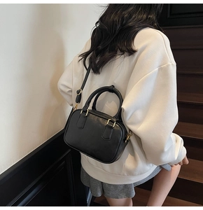 Fashionable black faux leather small square bag shown with adjustable shoulder strap and handle