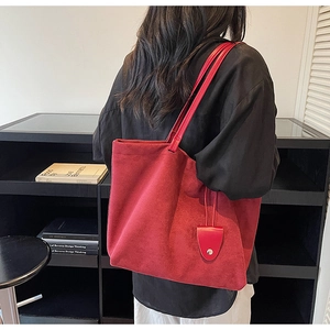 Detail view of large red suede tote bag with slim shoulder straps and matching charm