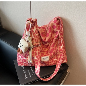 Detail of pink leopard print tote bag with plush toast charm on black leather seat