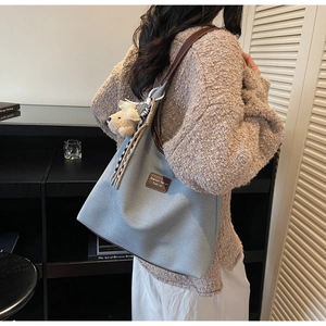 Vue latérale du grand sac cabas en toile bleu clair avec anses en cuir brun et breloque ours