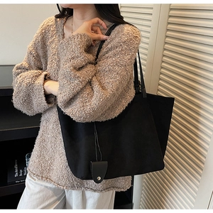 Detail of black suede tote bag with minimalist shoulder strap and metal snap charm