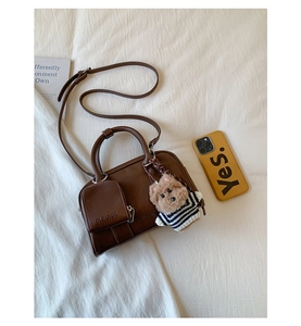 Brown leather Boston bag with a mini pouch and teddy bear charm on white fabric
