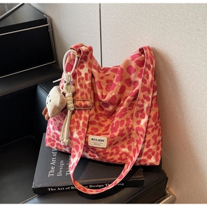 Pink leopard print tote bag with plush toast charm and logo patch on designer books