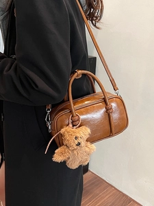 Brown vintage glossy leather Boston bag with teddy bear pendant worn by a model