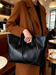 Close-up of a large black matte leather tote bag with dual shoulder straps and handles