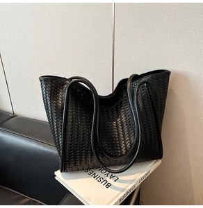 Detail of a large black woven tote bag with rounded handles on a white prop book