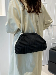 Chic black woven cloud bag with silver chain strap worn by a model in a beige coat
