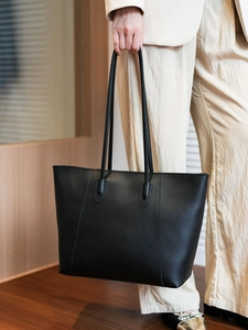 Close-up of black leather tote bag handle and stitching detail on a beige suit background