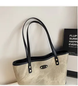 Detail of taupe suede tote bag with black leather handles and oval metal logo plate