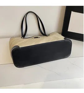 Close-up of beige tote bag with black leather base and metallic logo on marble surface