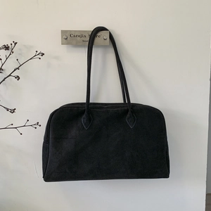 Détail d'un grand sac Boston en daim noir suspendu sur un mur au style minimaliste