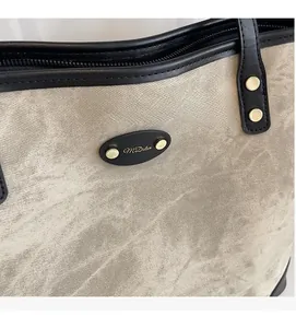 Detailed close-up of textured tote bag showing black leather trim and golden logo plate