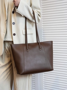 Close-up of a large brown leather tote bag with vertical stitching and long shoulder straps