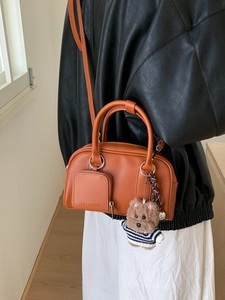Chic orange semi-cylindrical crossbody bag with front pocket and dog charm accessory