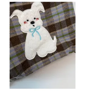 Detail of plaid tote bag featuring a cute white plush puppy patch with a blue bow