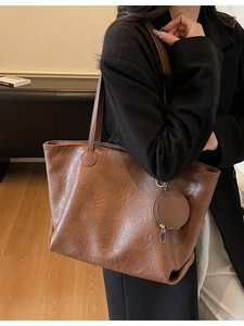Brown leather large tote bag with round coin purse shown on shoulder in office setting
