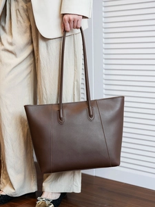 Close-up of a brown leather tote bag with vertical stitching and double shoulder straps