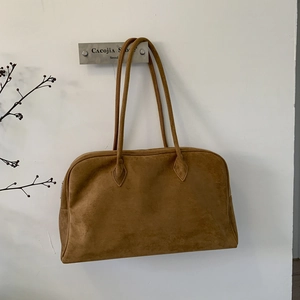 Gros plan détaillé de la texture d'un sac bandoulière en daim marron et doubles anses