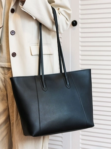 Minimalist large black tote bag with slender straps worn by model for office style