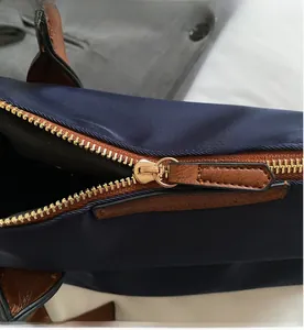 Dettaglio della cerniera in metallo dorato e finiture in pelle marrone sulla borsa in nylon