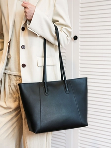 Detail shot of a large black leather tote bag worn with a chic cream-colored suit