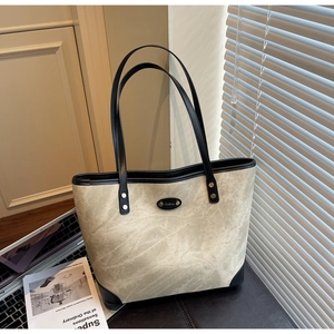 Detail of a large beige tote bag with black leather trim and handles on a desk