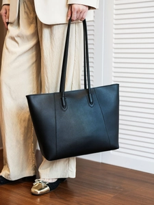 Close-up of a large black leather tote bag with long shoulder straps for office commute