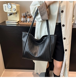 Close-up of a large black woven leather tote bag worn by a model in a cafe setting