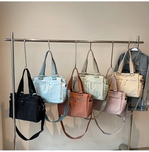 Detailed display of five colorful nylon tote bags with multiple zippers on metal rack