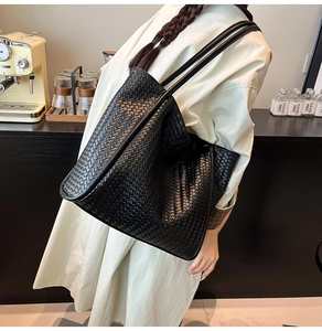 Close-up of the black hand-woven leather texture and long shoulder straps on the tote bag