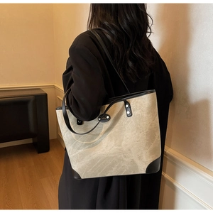 Detail of marble pattern tote bag with black leather trim worn by a model in warm light