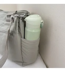 Close-up of light green nylon tote side pocket holding a water bottle with metallic zipper
