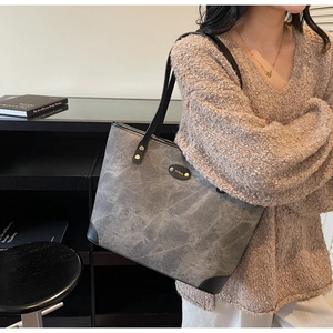 Detail of grey washed tote bag with black leather accents and metallic brand plate