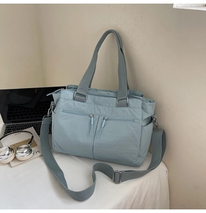 Detail of light blue nylon tote bag showing multiple zipper pockets and adjustable strap