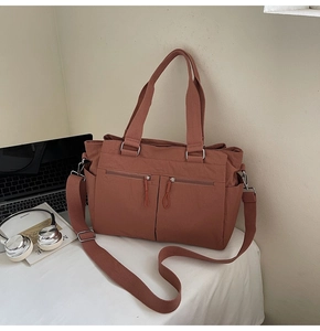 Detail of brick red nylon tote bag with dual front zippers and adjustable shoulder strap
