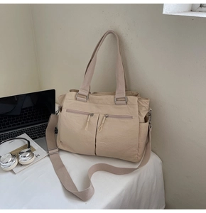 Detail view of khaki tote bag with front zipper pockets and laptop on a white desk