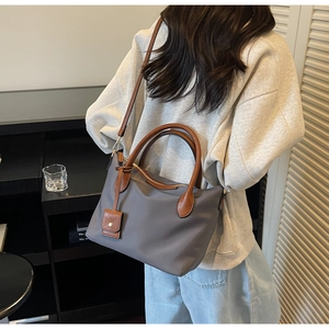 Dettaglio della borsa a secchiello in nylon grigio con cinturini in pelle marrone su modella