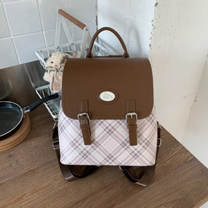 Detail of vintage-style backpack with plaid pattern and cute rabbit emblem on wooden desk