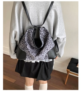 Detailed back view of a grey leopard print backpack with black leather straps on a model