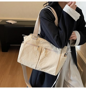 Detail of cream nylon tote bag with multiple zip pockets and adjustable strap shown on model