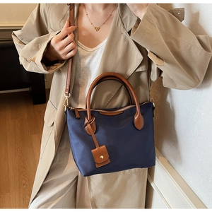 Dettaglio borsa tote in nylon blu scuro con manici in pelle marrone e tracolla regolabile