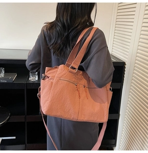 Detail of brick red nylon tote bag with functional zipper pockets and wide fabric strap